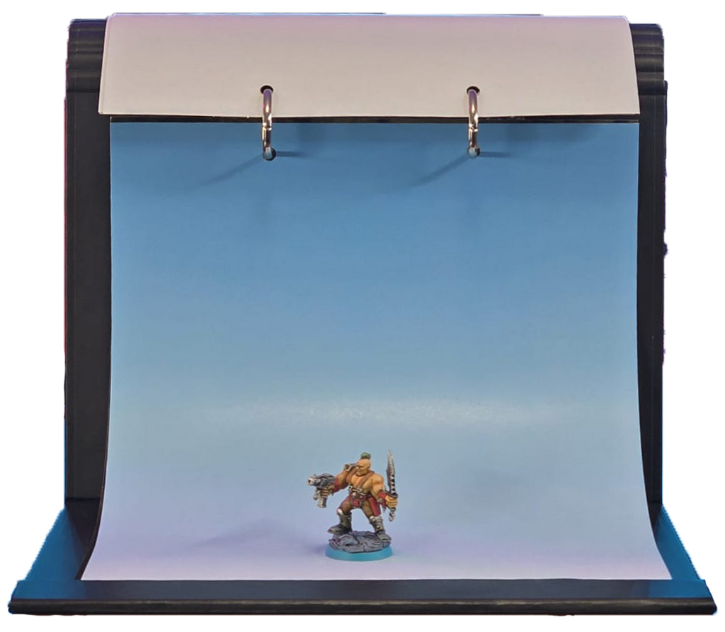 A miniature tabletop gaming scene setup featuring a small painted warrior figurine standing on a blue base, photographed in front of a curved blue gradient backdrop mounted on a black stand with a white top panel.